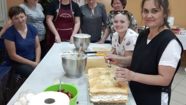 Zdjęcie przedstawia osoby biorące udział w warsztatach kulinarnych w trakcie dekoracji tortu.
