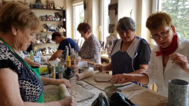 Zdjęcie przedstawia seniorki siedzące przy stole tworzące ceramiczne medale.