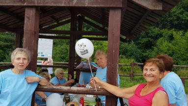 Zdjęcie przedstawia grupę seniorów w plenerze; jedna pani trzyma balon z logiem "Działaj Lokalnie".