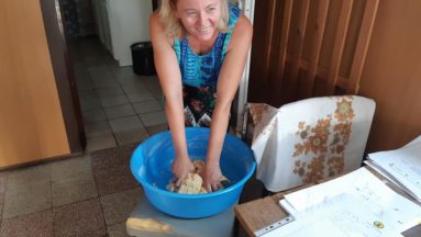 Zdjęcie przedstawia kobietę we wnętrzu, wyrabiającą ciasto w misce.