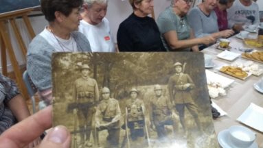Grupa kobiet przy stole oglądających archiwalne zdjęcia, na zdjęciach żołnierze z karabinami
