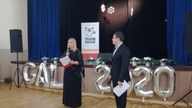 Zdjęcie przedstawia dwie osoby, stojące przed sceną, podczas gali. W tle widać napis GALA 2020 ułożony z balonów oraz rollup z logiem "Działaj Lokalnie".