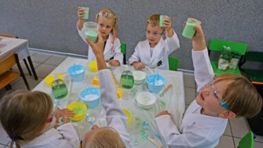 Grupa dzieci ubrana w kitle podnosi kubki z gotowym mydłem