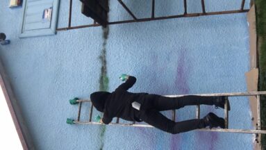 Osoba stoi na drabinie i maluje mural.