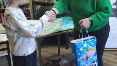 Zdjęcie przedstawia kobietę i chłopca. Kobieta gratuluje chłopcu i wręcza mu nagrodę.