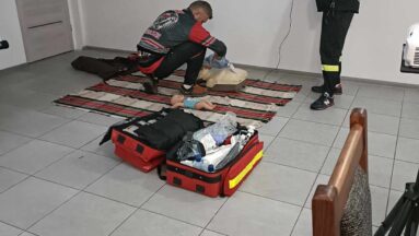 Mężczyzna nadzoruje ćwiczenie drugiego polegające na resuscytacji manekina ułożonego na podłodze