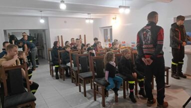 Dzieci i młodzież siedzący na krzesełkach w sali w skupieniu słuchają prowadzących spotkanie