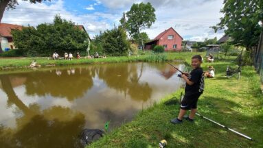 Chłopiec z wędką stoi nad zalewem.