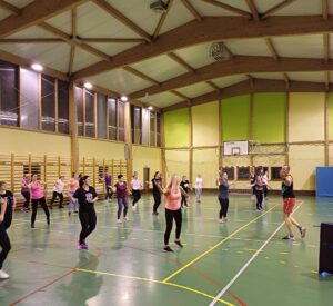zumba-3 Zajęcia Zumby - na zdjęciu grupa kolorowo ubranych osób ćwiczących przy rytmicznej muzyce; aktywne ćwiczenia prowadzi instruktor Zumby.