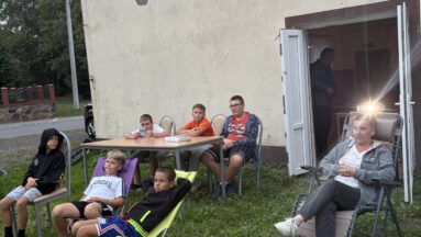 Uczestnicy projektu spędzają czas na świeżym powietrzy. Siedzą na ławce i leżakach przed budynkiem