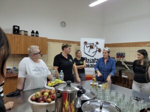 ziolowy-urok-dnia-codziennego-_spotkanie-2_3.jpg Uczestnicy warszatatów stoją w sali przed stołami. Za nimi znajduje się rollup Programu Działaj Lokalnie