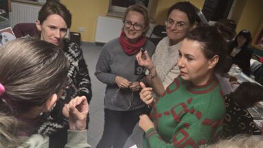 Inspirujące rozmowy z ekspertami - zdjęcie prezentuję grupę uśmiechniętych pań podczas rozmowy z ekspertką naturopatką, niektóre osoby robią notatki.