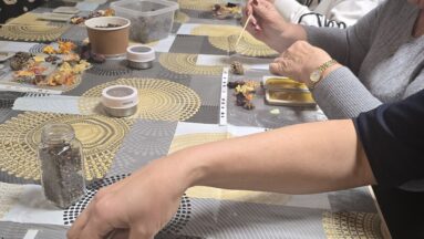 Warsztaty tabliczki florenckie - zdjęcie przedstawia grupę osób siedzącą przy stole pełnym produktów naturalnych, ziół i roślin, trwa praca nad woskowymi zapachowymi tabliczkami florenckimi.